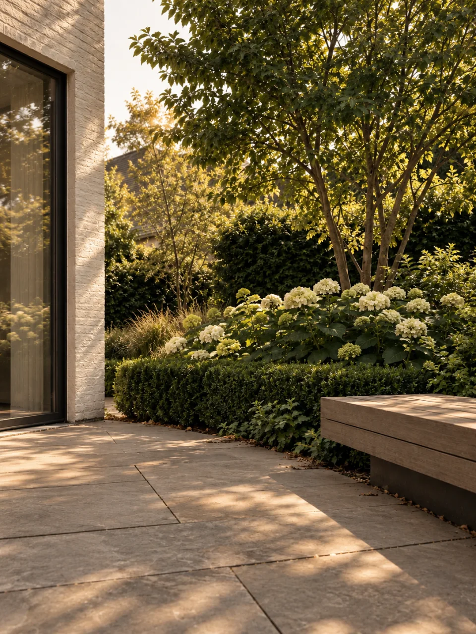 Een natuurstenen terras met een houten bank en een aangelegde plantenborder